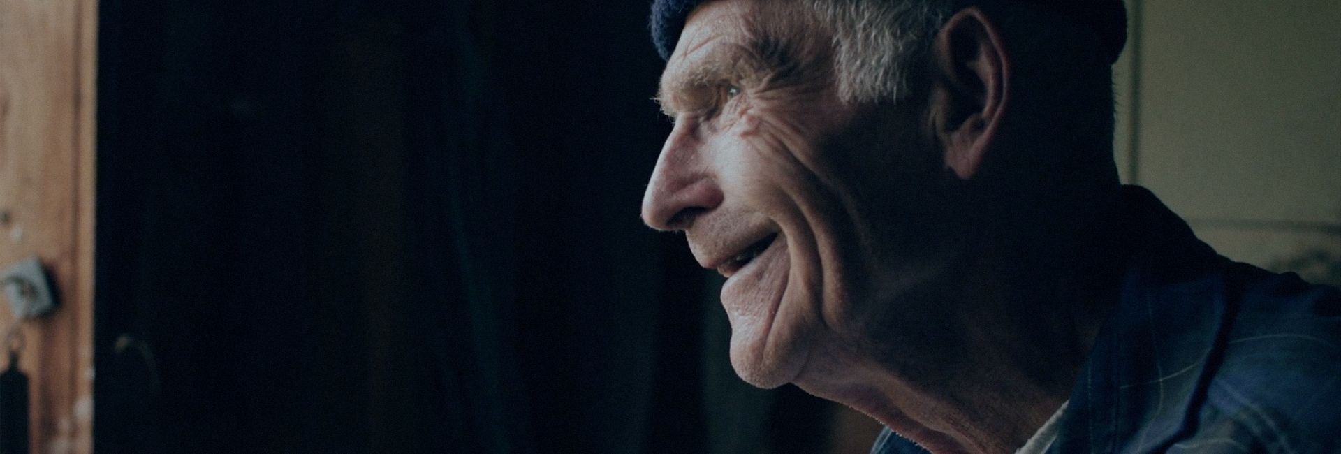 En eldre mann ser smilende ut vinduet
