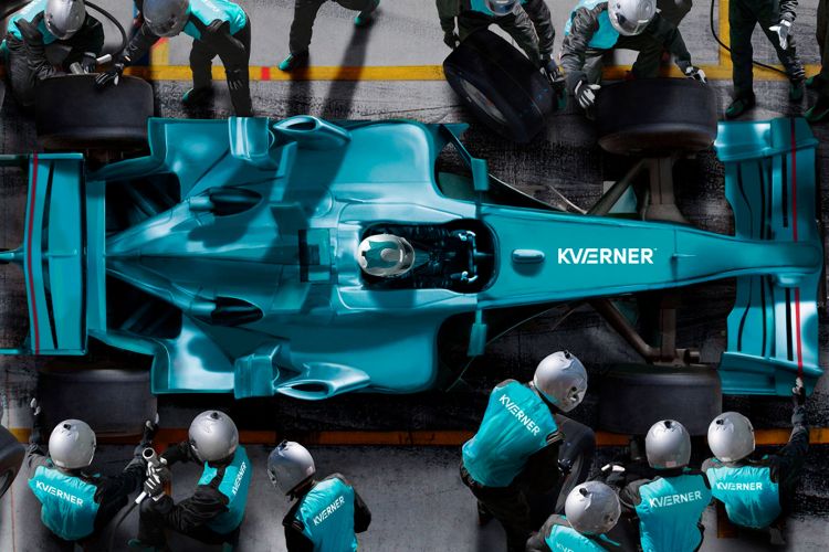 En turkis formel1-bil sett ovenfra med Kværner-logo på panseret. Bilen er inne i pitstop'en og får overhaling av teamet.